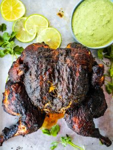 Peruvian Spatchcock Chicken with Aji Verde Sauce is plated with sauce, limes, and more cilantro.