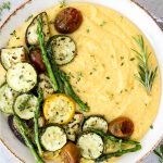 Roasted Italian Vegetables with Parmesan Polenta is plated in a white bowl and topped with fresh herbs.