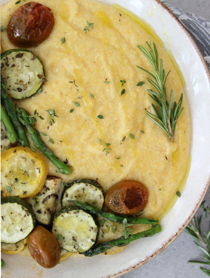 Roasted vegetables are plated over parmesan polenta in a white bowl.