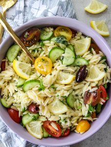 Italian Lemon Orzo Salad is plated in a purple bowl with a gold stone.