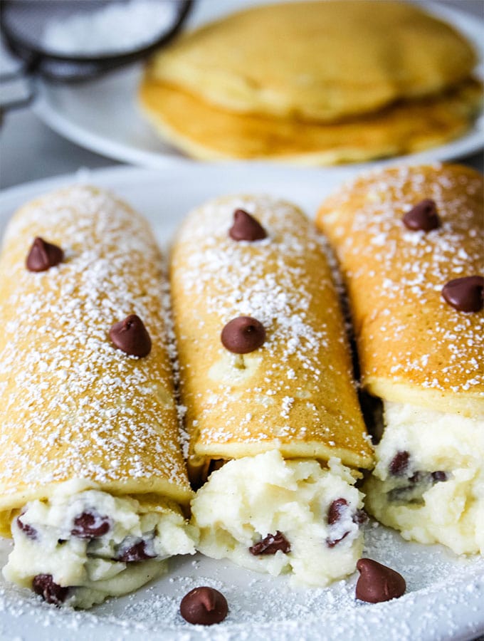 Cannoli stuffed buttermilk pancakes are topped with powdered sugar and chocolate chips.