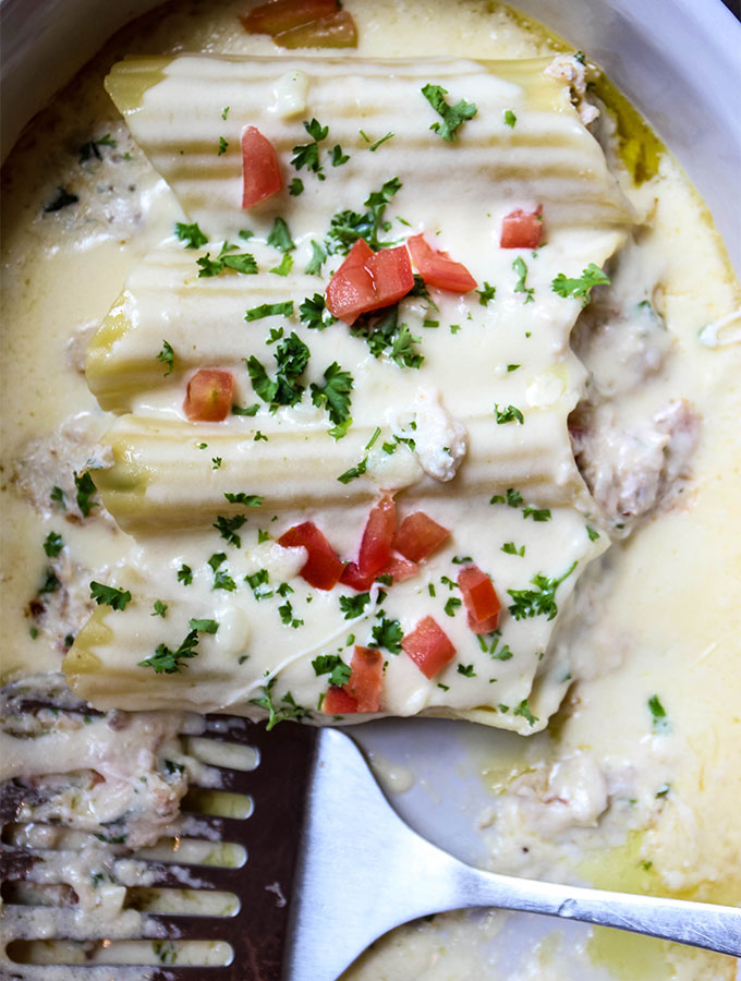 Crab Stuffed Manicotti with Alfredo Sauce is baked in a dish and served with a spatula.