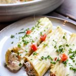 Crab Stuffed Manicotti with Alfredo Sauce is plated on a white plate and topped with parsley.