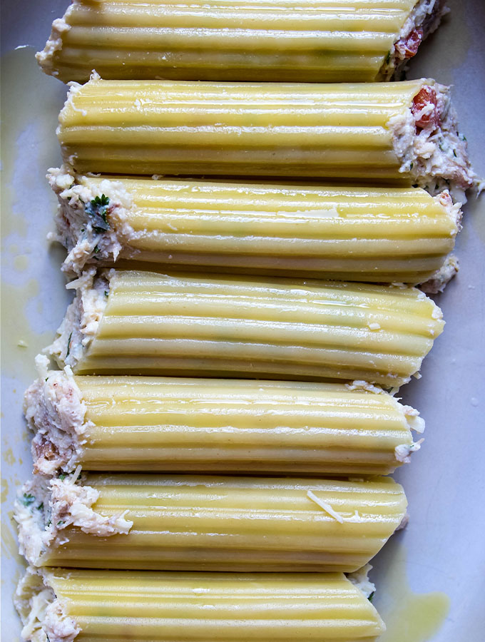 Crab Stuffed Manicotti with Alfredo Sauce is placed in a baking dish to cook.