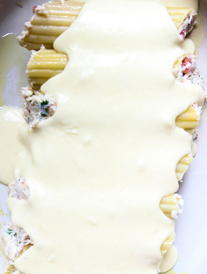 Crab Stuffed Manicotti with Alfredo Sauce is placed in a baking sheet and smothered with alfredo sauce.