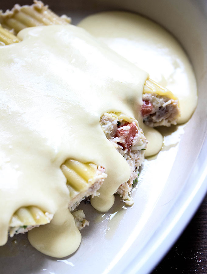 Crab Stuffed Manicotti with Alfredo Sauce is smother in alfredo sauce in a baking sheet.