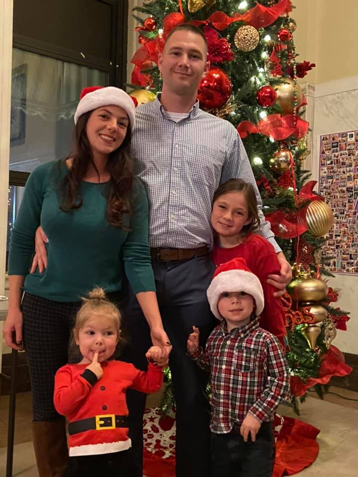 The Brubaker family is posed with Santa hats in front of a Christmas tree.