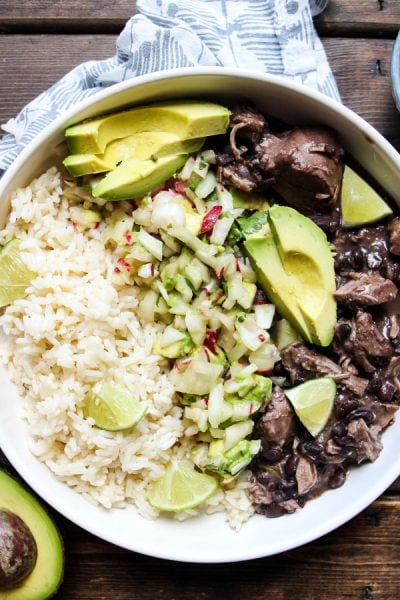 Frijol con Puerco (Mexican Pork and Beans) is plated in a white bowl with avocado slices.