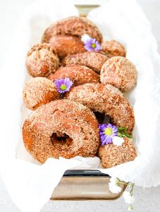 Apple cider donuts are lined in a bowl and topped with fresh flowers.