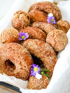 Cider donuts are placed in a parchment paper lined bowl and topped with flowers.