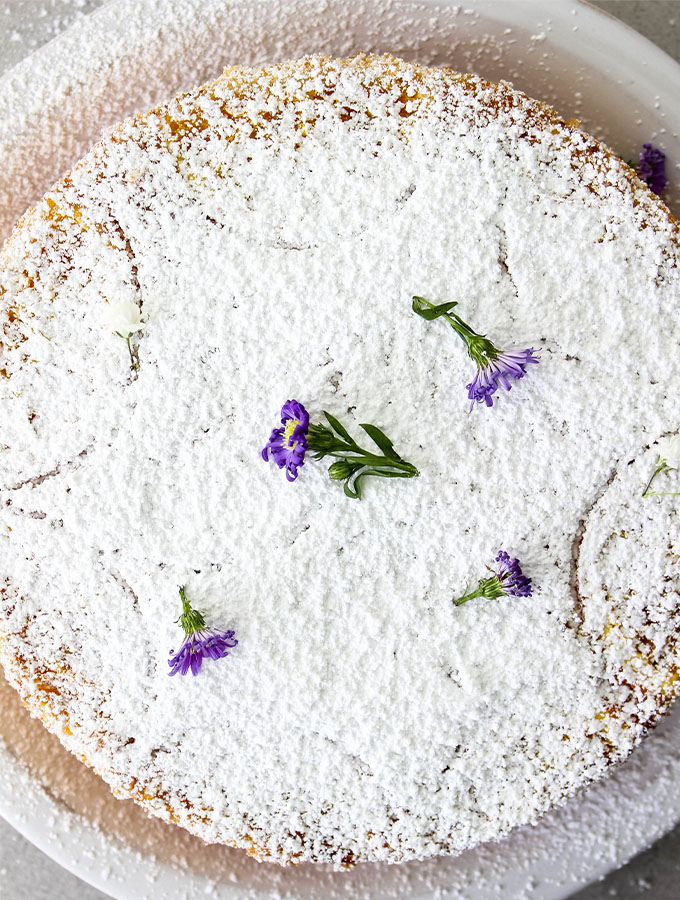 Easy Italian Olive Oil Cake is topped with sugar and flours on a white plate.