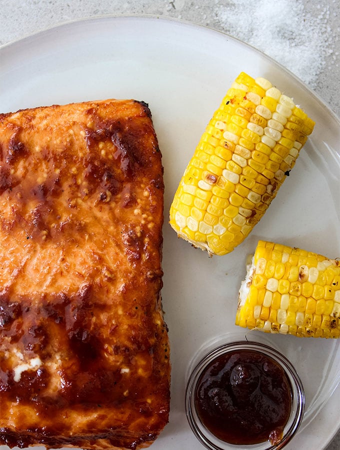 Grilled Bourbon Glazed Salmon is plated with corn and extra bourbon BBQ sauce.