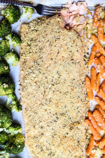 Salmon is laid in between carrots and broccoli on a sheet pan.
