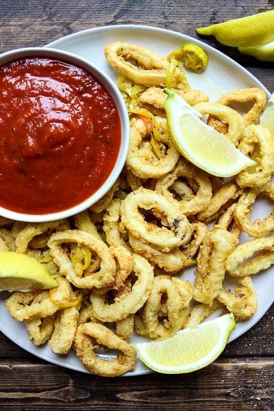 Rhode Island style calamari is plated with marinara sauce and lemon wedges.