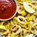 Rhode Island style calamari is plated with marinara sauce, lemon wedges, and banana pepper rings.