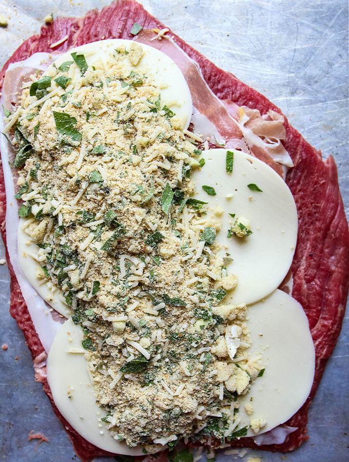 A flank steak is layered with prosciutto, provolone cheese, and a breadcrumb mixture before it is rolled into a braciole.