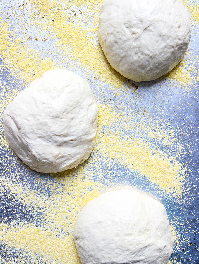 Margherita Pizza dough is placed on top of corn meal and allowed to rest.