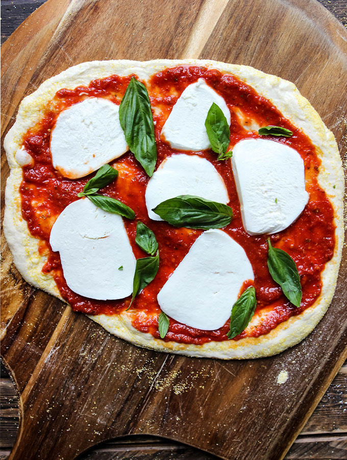 Margherita Pizza dough is stretches, then topped with sauce, mozzarella cheese, and fresh basil.