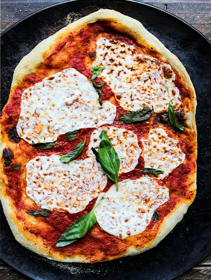 Margherita Pizza is cooked on a pizza pan in the oven at 500 degrees.