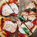 Margherita Pizza is sliced into triangles on a wooden pizza peel.the pizza peel.