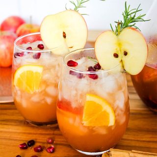 Autumn harvest sangria is topped with sliced apples, pomegranate arils, and fresh rosemary for a beautiful drink.