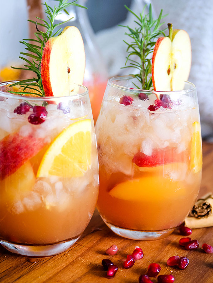 Autumn harvest sangria is poured into cups and topped with apple slices, pomegranate arils, and fresh rosemary sprigs.