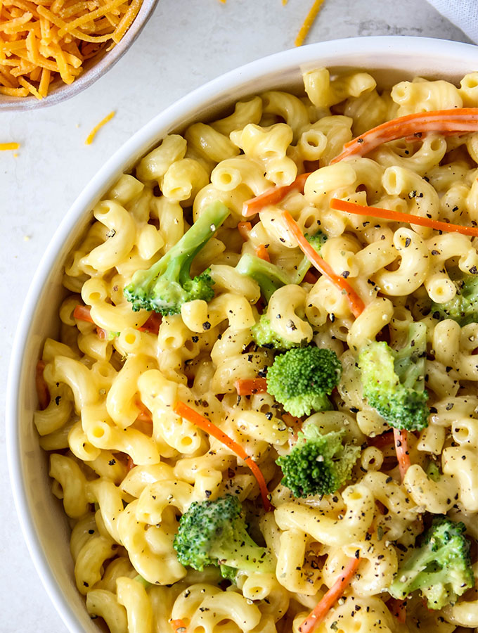 Broccoli cheddar mac and cheese is plated in a white bowl and topped with cracked pepper.