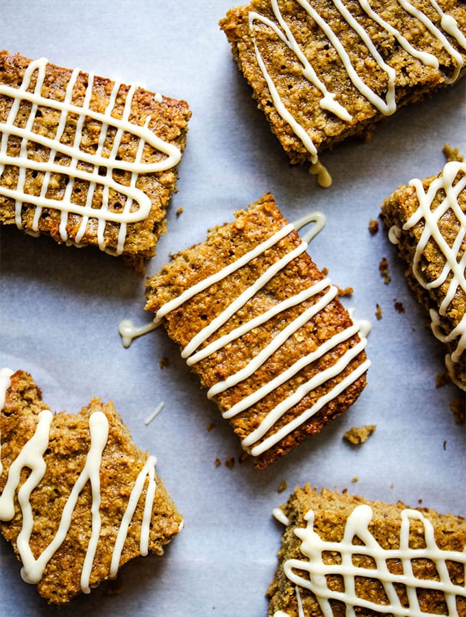 The banana oatmeal breakfast bars are drizzled with maple cream cheese frosting on parchment paper.