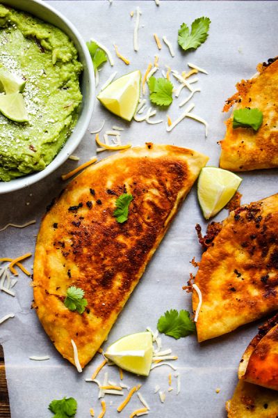 Margarita guacamole is plated next to the quesadillas and topped with cheese and limes.