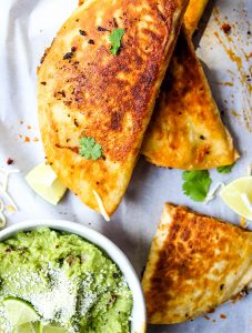 The chorizo sausage quesadillas are stacked on parchment paper next to a bowl of margarita guacamole.