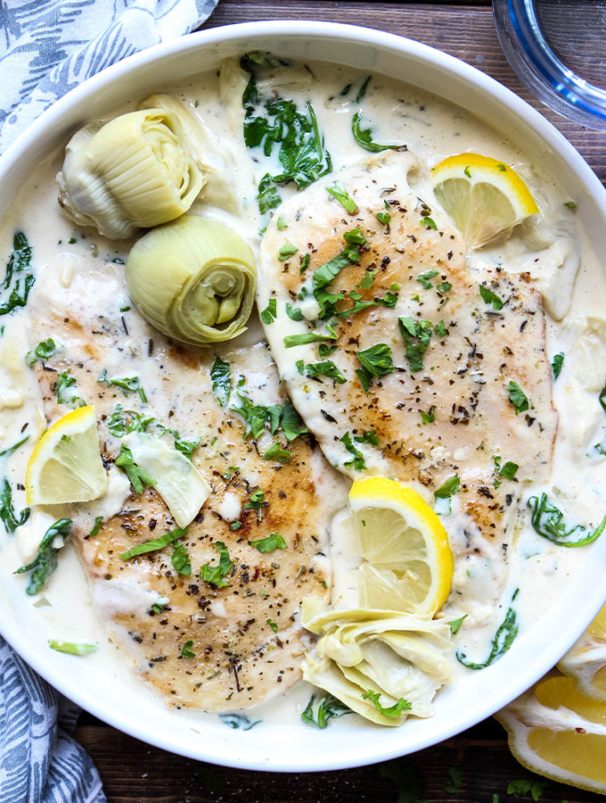 Chicken breasts are plated on top of the artichoke and spinach sauce then topped with more artichokes, lemons, and parsley.
