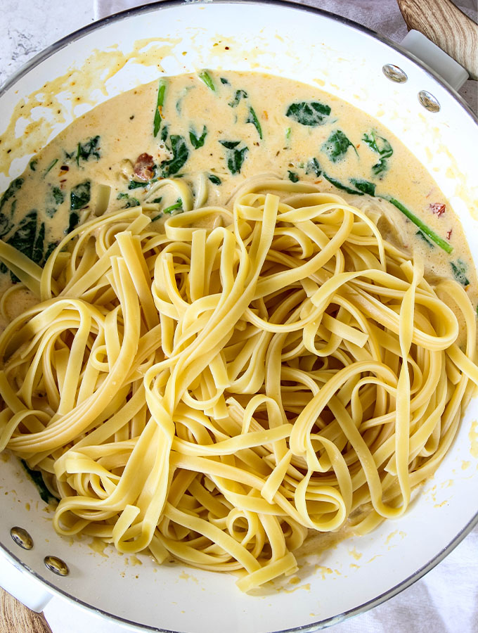 The linguine pasta is tossed in the pan that the cream sauce was built in before tongs toss the pasta in it.