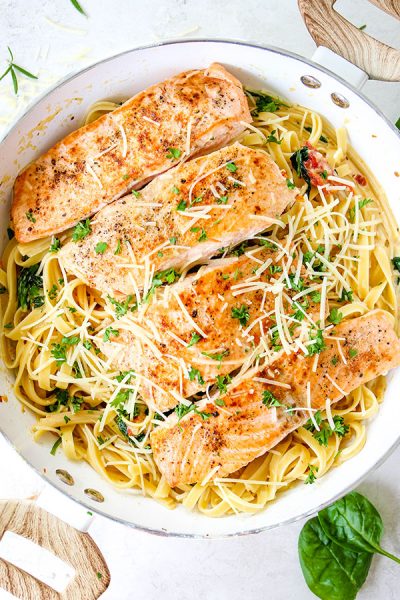 Salmon is placed on top of the pasta and topped with parmesan cheese and fresh chopped parsley.