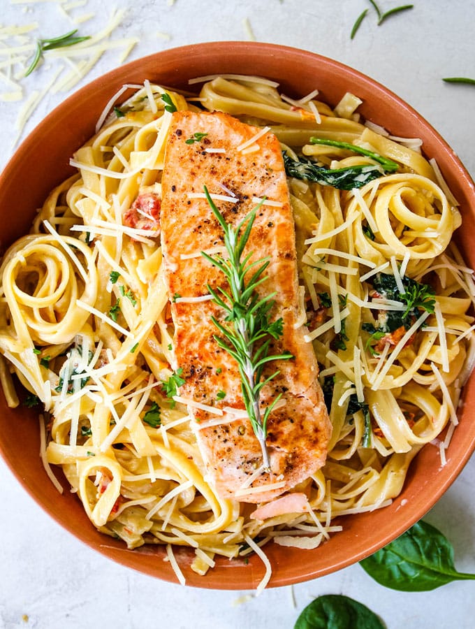 A sprig of fresh rosemary is placed on top of the pan seared salmon and creamy pasta.