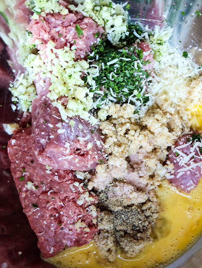 Pork, beef, veal, eggs, breadcrumbs, and cheese is combined in a bowl to create the meatballs.