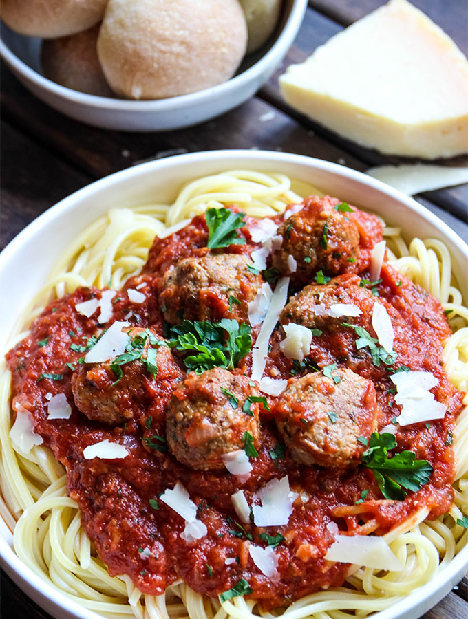 Italian meatballs and sauce is spooned over spaghetti pasta and topped with cheese and parsley.