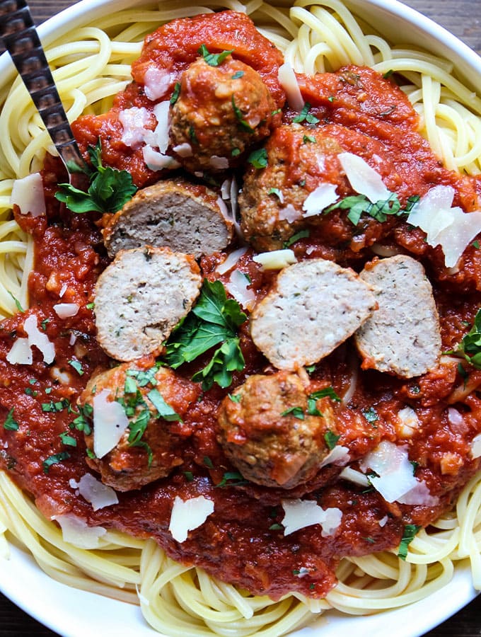 Italian meatballs are sliced in half on top of spaghetti pasta to show tender texture.