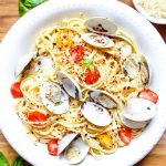 Linguini with clams is plated in a white bowl and topped with red pepper flakes and fresh basil.