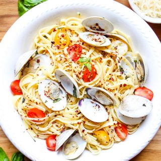 Linguini with clams is plated in a white bowl and topped with red pepper flakes and fresh basil.