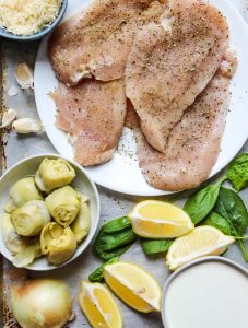 Spinach and artichoke chicken skillet ingredients are displayed individually in a sheet pan.