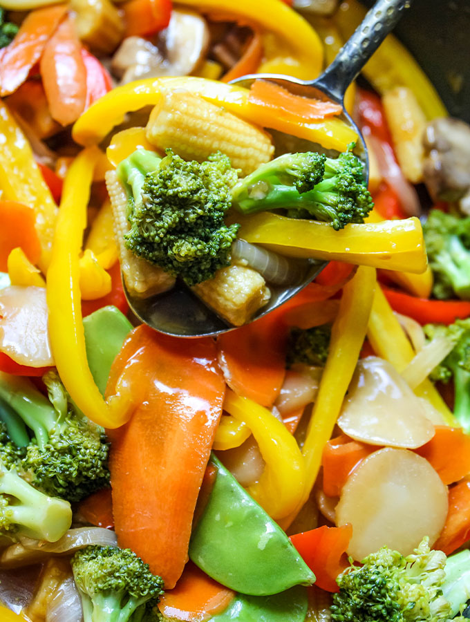 A spoon is holding up a spoonful of stir fry vegetables that were cooked in the stir fry sauce.