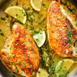 Chicken breasts are placed in the white wine pan sauce and topped with more fresh herbs and lemon wedges.