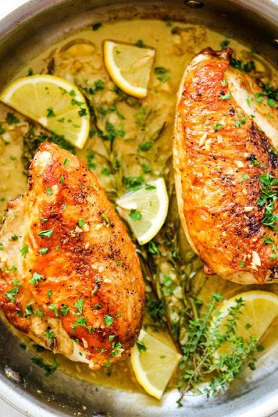 Chicken breasts are placed in the white wine pan sauce and topped with more fresh herbs and lemon wedges.