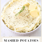 Mashed potatoes are plated in awhite bowl and topped with cracked pepper, butter, and fresh herbs.