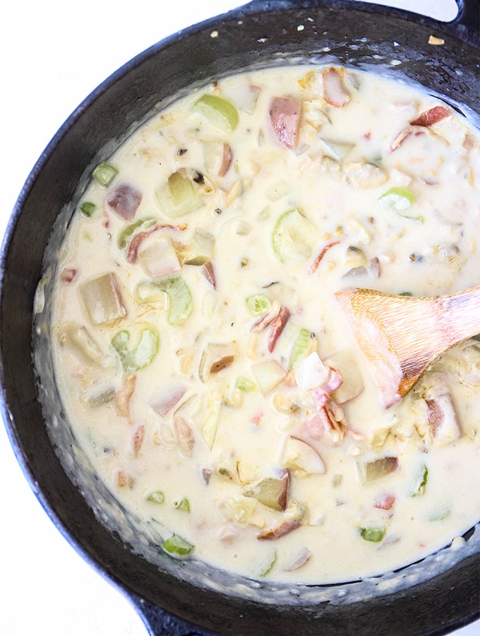Clam chowder is cooked in a cast iron dutch oven and stirred with a wooden spoon.