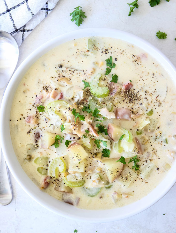 Clam chowder is plated in a white bowl and topped with cracked pepper and fresh parsley.