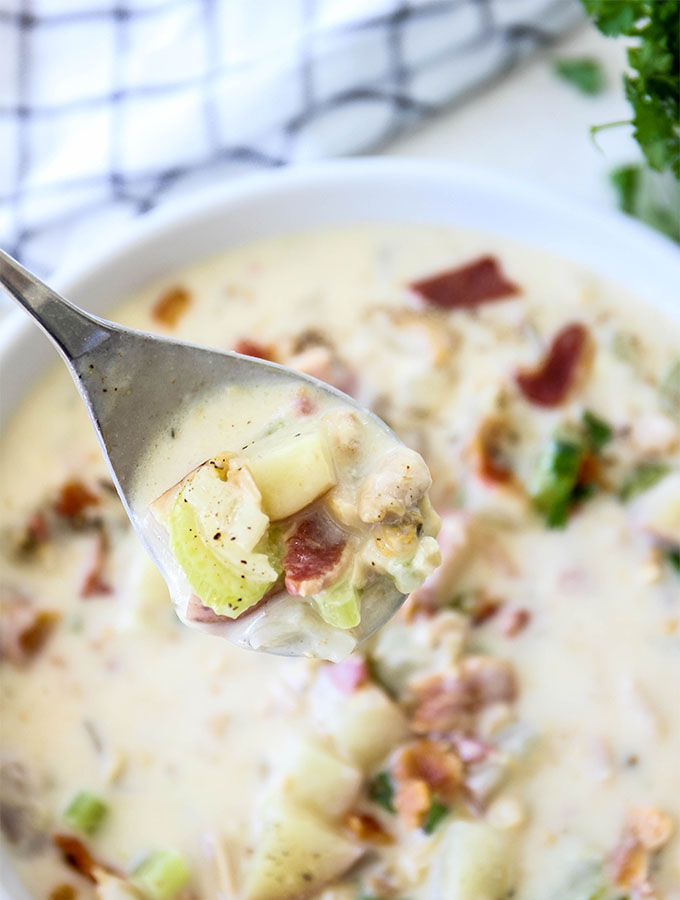 A spoon is lifting a big, hearty biteful of celery, bacon, clams, and the soup base.