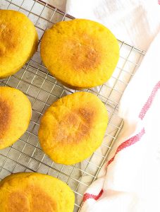 Pumpkin English muffins are cooled on a wire cooling rack on top of a kitchen towel.