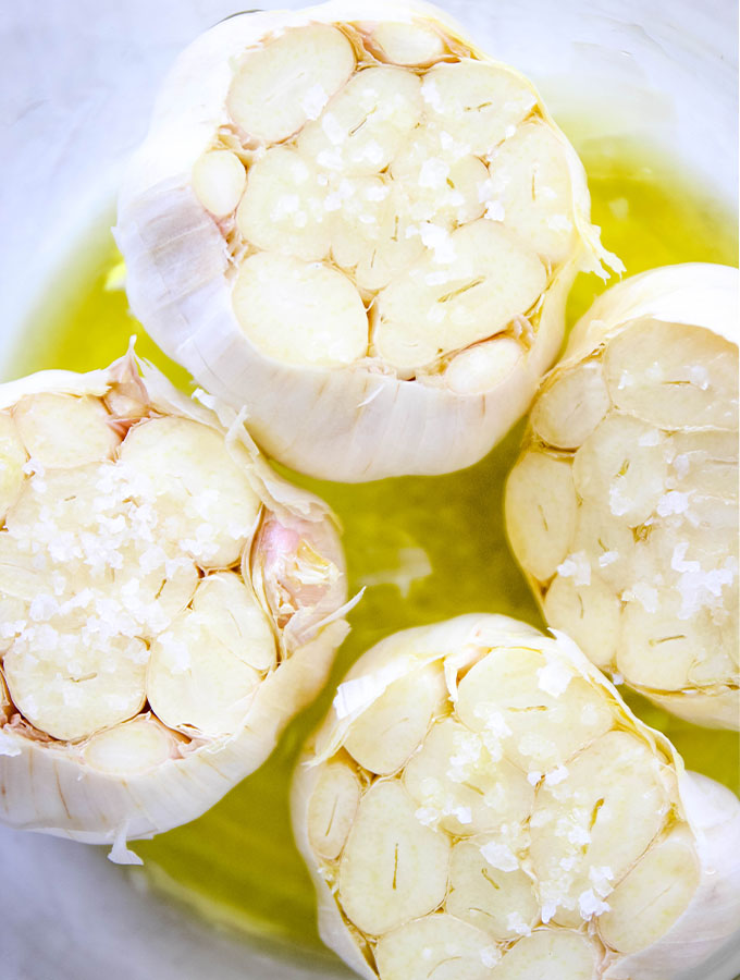 Raw halved garlic heads are drizzled with olive oil and sprinkled with coarse salt.