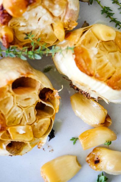 Cloves of roasted garlic are pulled out of the garlic head and plated with fresh herbs.